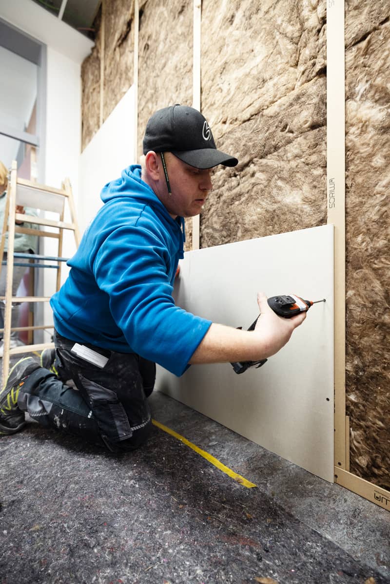 Mitarbeiter montiert eine Gipskartonplatte an einer Trockenbauwand mit SORIWA Multi Profilen und Dämmung im Hintergrund.